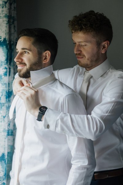 Groom getting ready putting on suit and tie groomsman helps