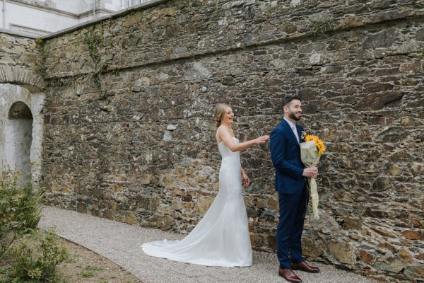 Groom holding sunflowers bride behind him tapping shoulder