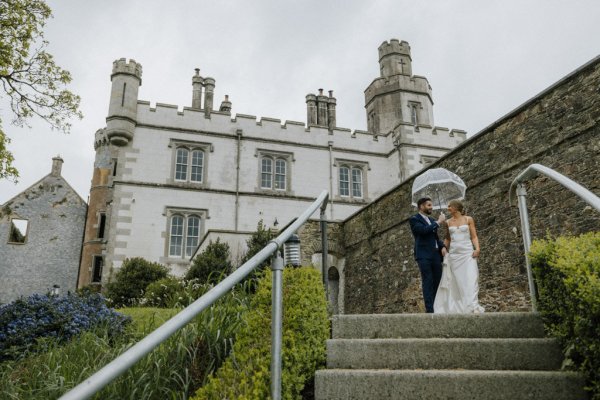 Bride and groom hold umbrella exterior wedding venue rainy shot