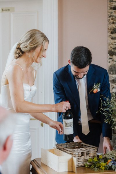 Bride and groom hold bottle of wine at table