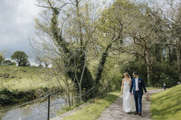 Bride and groom walk beside canal exterior park shot trees and grass