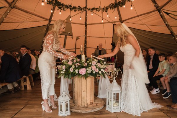 Bride and bride officiant at alter under marquee tent lighting candles lights above