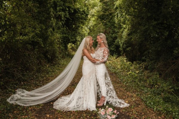 Bride and bride standing in forest hugging each other