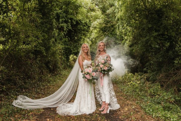 Bride and bride dress detail standing in forest holding hands bouquet of flowers smoky background fog