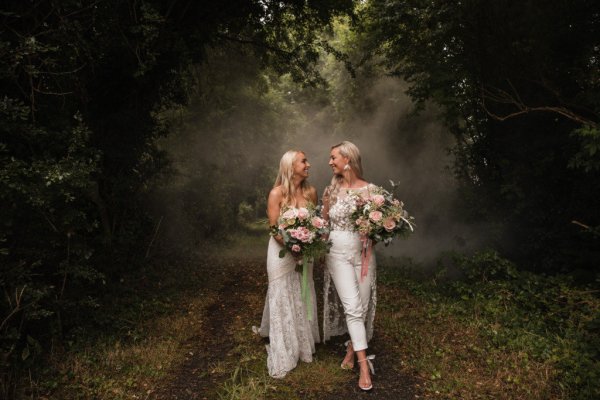 Bride and bride dress detail standing in forest holding hands bouquet of flowers