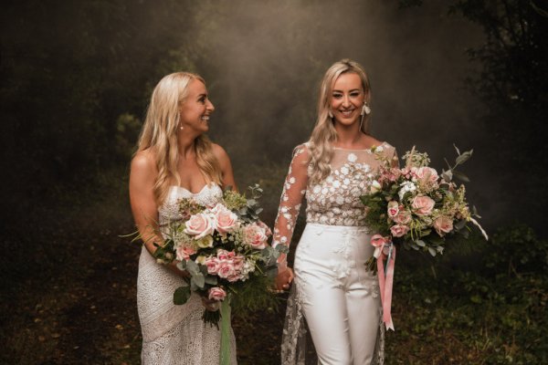 Bride and bride dress detail standing in forest holding hands bouquet of flowers