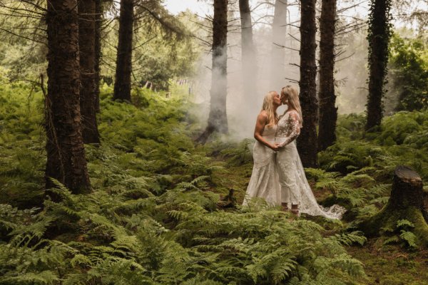 Bride and bride couple holding hands in forest trees in background