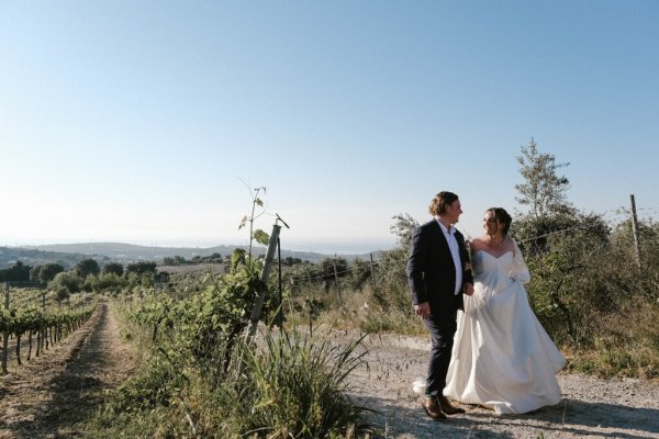 Bride and groom walk along cliff setting grass sunshine mountain landscape pathway plants grass