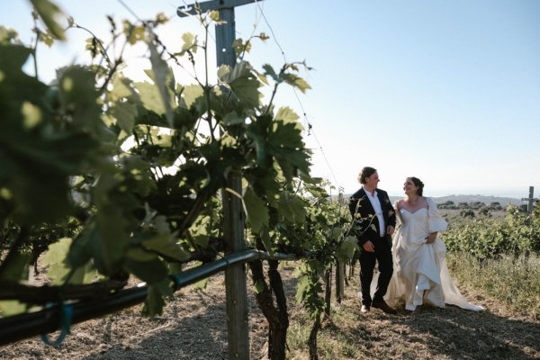 Bride and groom walk along cliff setting grass sunshine mountain landscape pathway plants grass