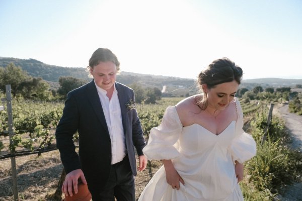 Bride and groom walk along cliff setting grass sunshine mountain landscape pathway plants grass