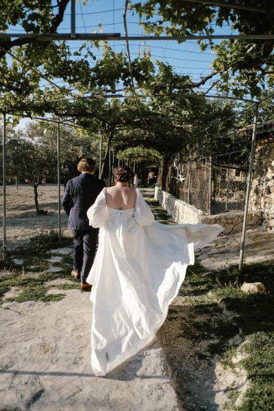 Bride and groom walk along cliff setting grass sunshine mountain landscape pathway plants grass