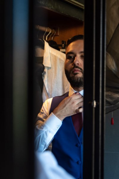 groom putting on tie in mirror