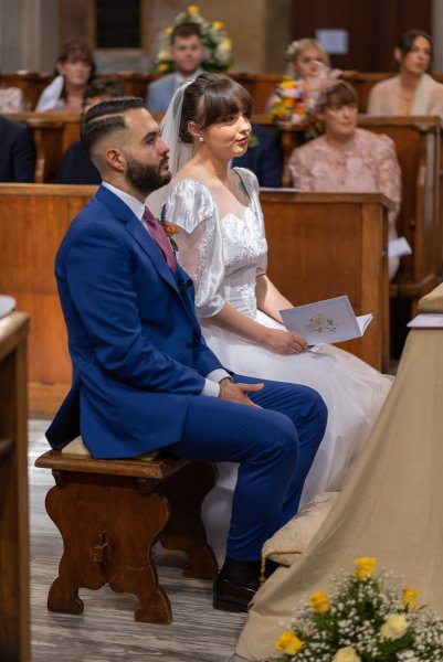 Bride and groom at alter inside cathedral sitting down in front of priest