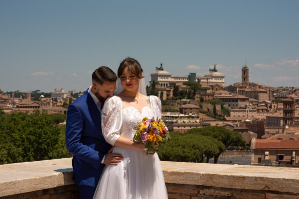 Roman landscape in background couple in foreground groom hugging bride from behind