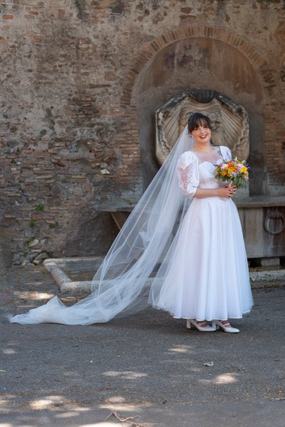 Bride in front of Roman statue fountain myth God holding bouquet of flowers