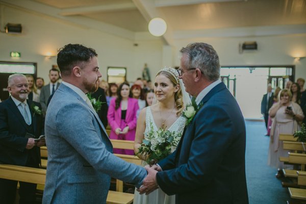 father of the bride at the alter with guests in background shakes grooms hand