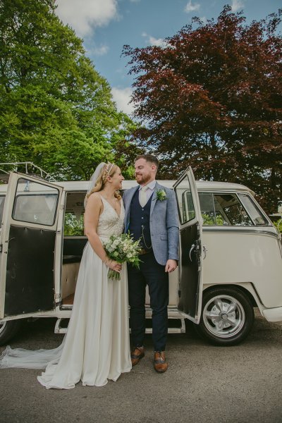 Bride and groom standing outside white wedding car looking at each other