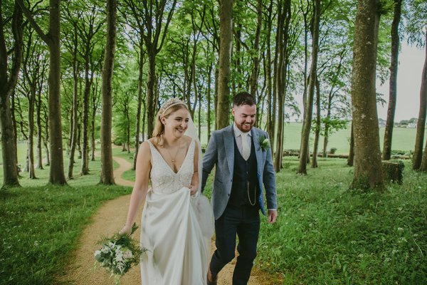 Bride and groom walking through park hand in hand