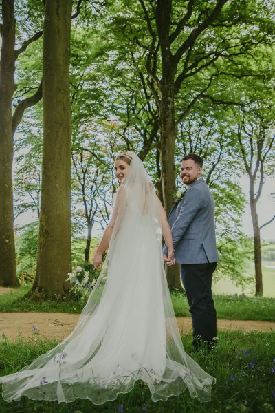 Bride and groom walking through park hand in hand