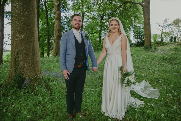 Bride and groom walking through park hand in hand