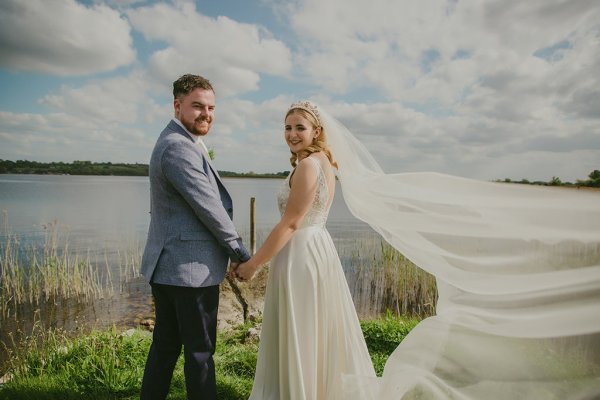 Bride and groom look over their shoulder lake in background