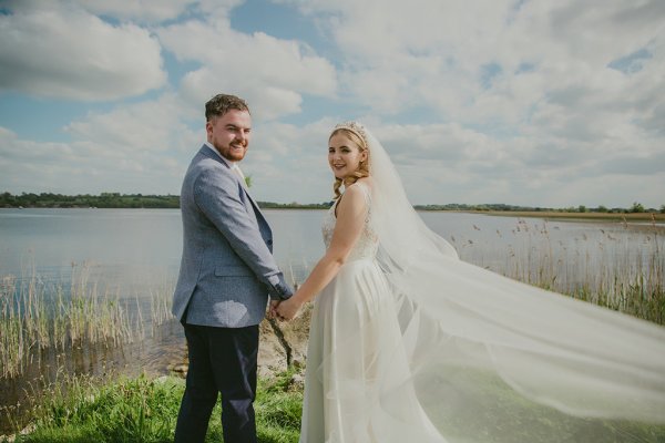 Bride and groom look over their shoulder lake in background