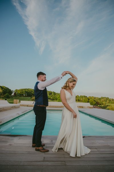 Bride and groom standing beside hotel swimming pool dancing