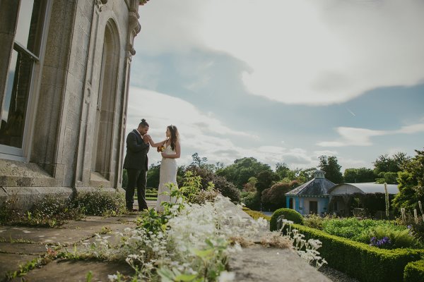 White flowers groom kisses brides hand outside wedding venue setting