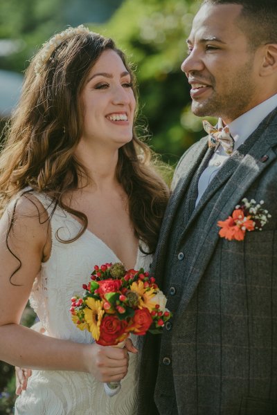 Close up shot of bride and groom holding red and orange flowers/bouquet