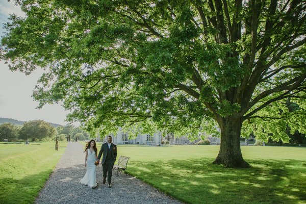 Bride and groom walk through forest/park hand in hand pathway