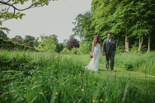 Bride and groom walk through forest/park hand in hand on grass