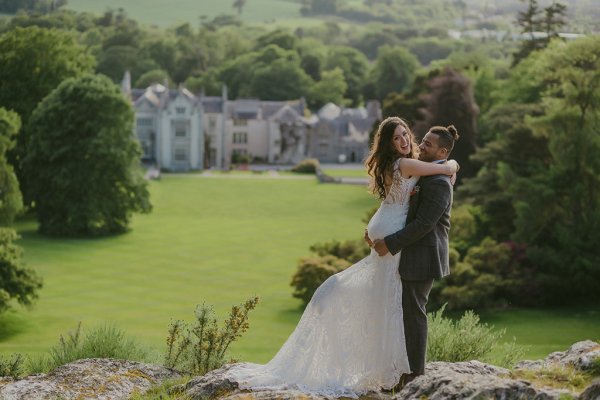 Killruddery house wedding venue in background groom picks up bride on grass