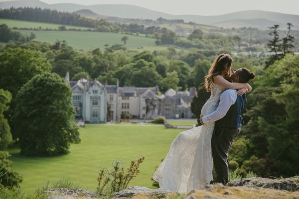 Killruddery house wedding venue in background groom picks up bride on grass