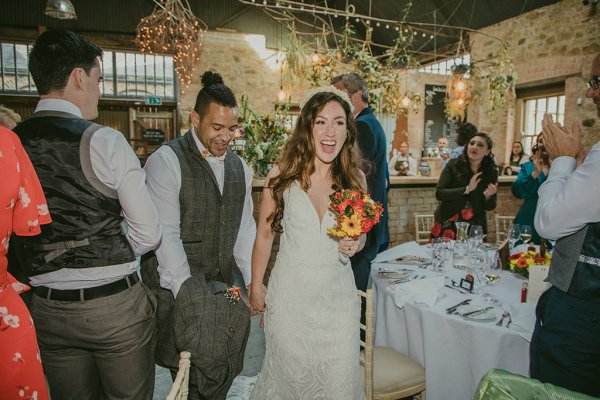 Couple enter dining room with guests orange and red bouquet in hand