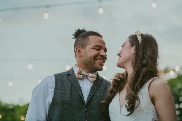 Bride and groom smile at each other lights in background