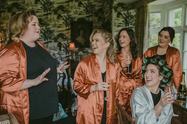 Orange satin bridalwear bridesmaids cheers champagne and bride laughing