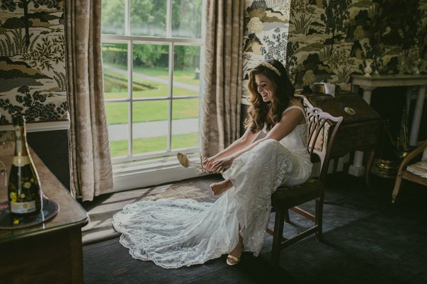 bride sitting beside window putting on wedding heels/shoes