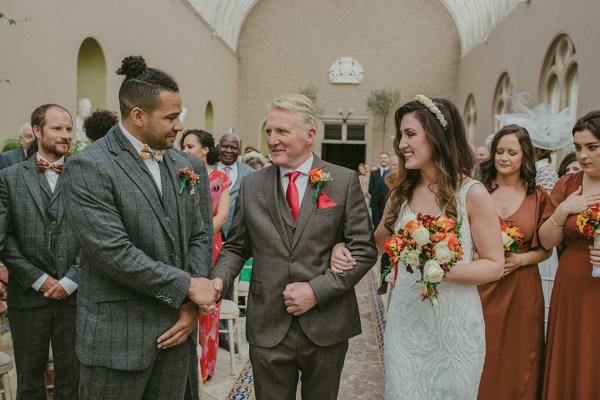 Bridesmaid groom and bride orange and yellow roses/flower bouquet kiss on the cheek couple father shakes grooms hand