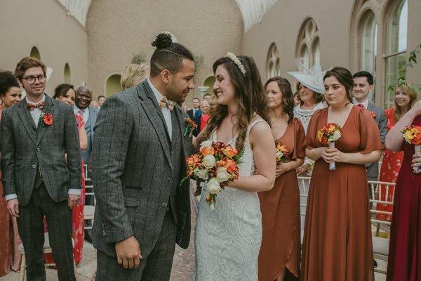 Bridesmaid groom and bride orange and yellow roses/flower bouquet kiss on the cheek couple