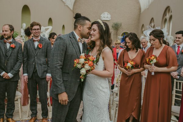 Bridesmaid groom and bride orange and yellow roses/flower bouquet kiss on the cheek couple