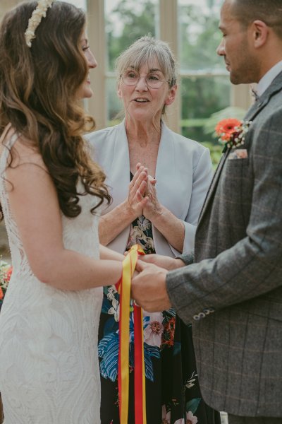 Bride groom red and yellow ribbon bound and officiant at alter