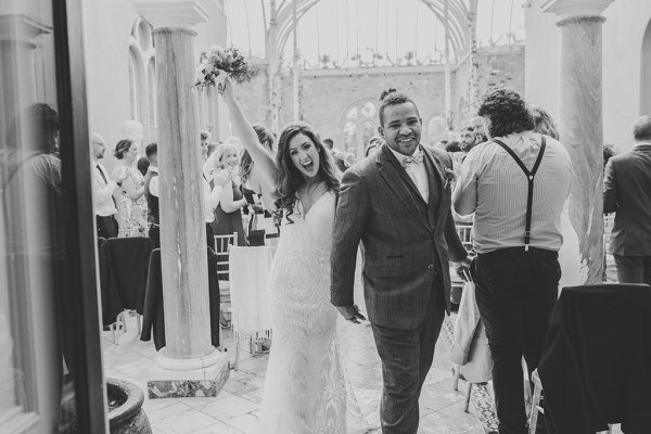 Bride hand in the air holding flowers just wed guests seated clapping black and white