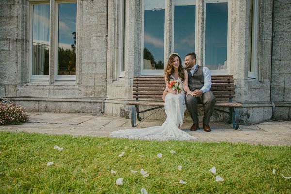 Bride and groom sit on bench outside wedding venue window grass shot