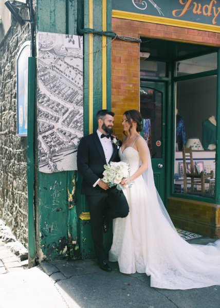 Bride and groom lean against wall in town