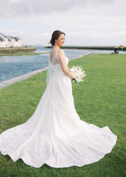 Bride standing on grass in front of lake