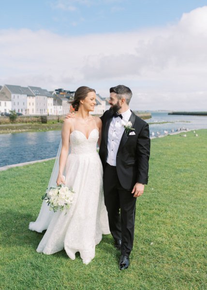 Bride and groom standing on grass in front of lake