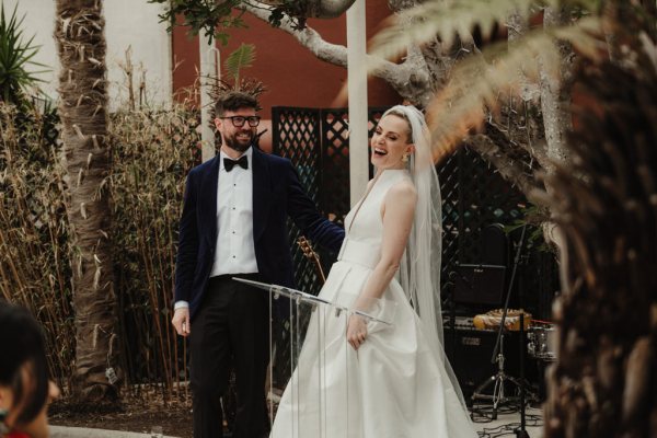 Bride wearing veil reads speech to guests and laughs/laughing