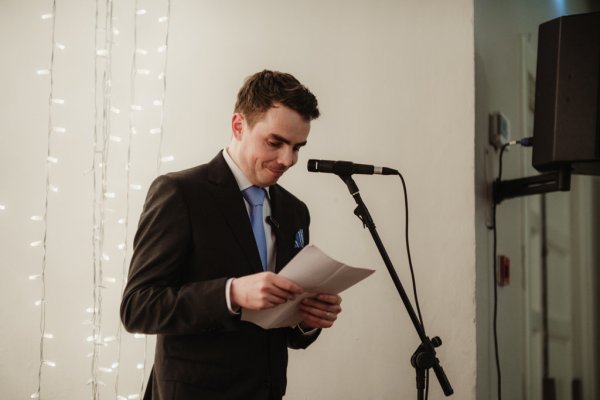 Man wearing blue tie and black suit reads speech microphone