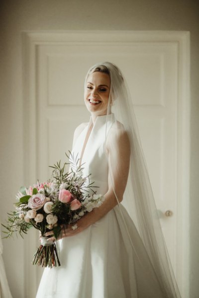 Bride smiles veil and bouquet in hand detail