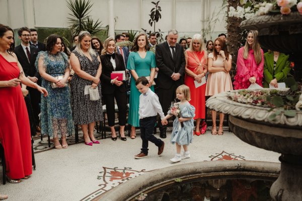 Two little children boy and girl hold hands walking down the aisle